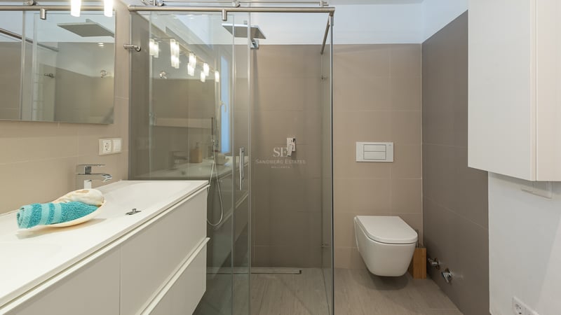 Salle de bain moderne avec meuble blanc, paroi de douche en verre et toilettes suspendues avec carrelage neutre.