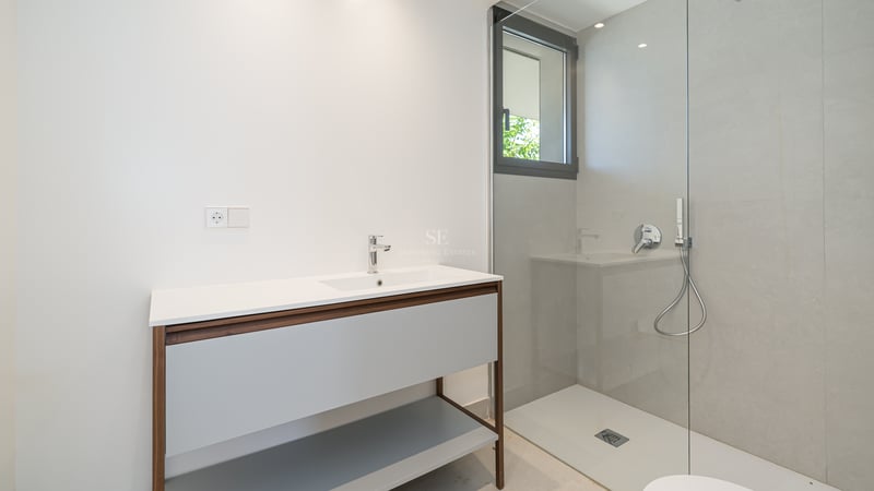 Baño moderno con lavabo de madera, ducha italiana de cristal y azulejos grises de gran formato.
