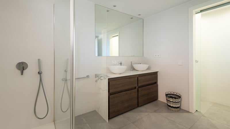 Salle de bain moderne et lumineuse avec meuble double en bois, plan en marbre, deux vasques et douche en verre.