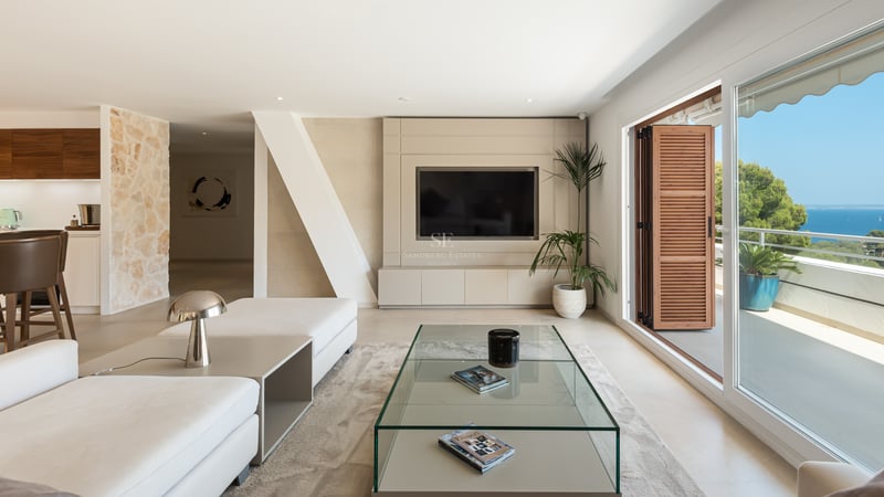 Salon contemporain lumineux avec canapés blancs, table en verre et grandes baies vitrées ouvrant sur la mer Méditerranée.