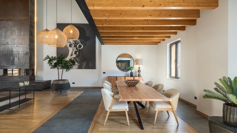 Salle à manger élégante avec table en bois massif, chaises rembourrées et grandes poutres en bois au plafond.