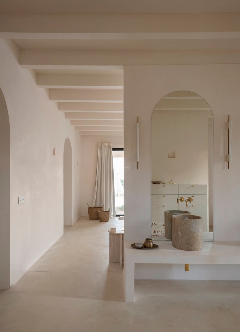 Minimalist bathroom with arched mirror, cylindrical stone sink, and exposed ceiling beams in sand tones.