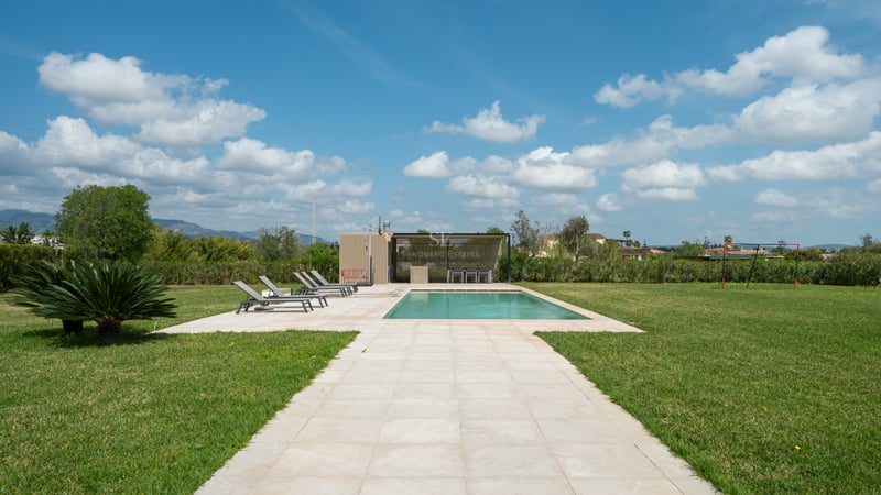 Piscine rectangulaire turquoise entourée de dalles en pierre, chaises longues, vaste pelouse et bar extérieur.
