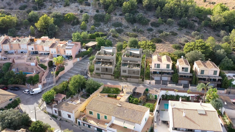 Vue aérienne de deux villas contemporaines grises entourées de maisons méditerranéennes traditionnelles en colline.