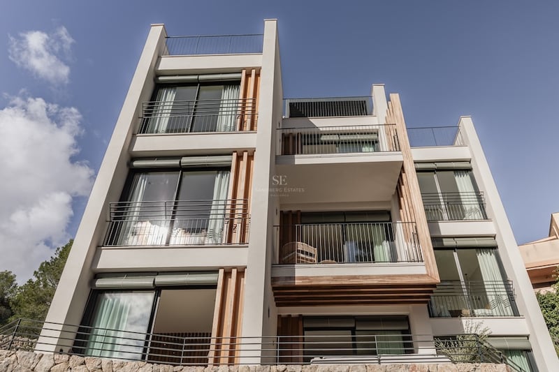 Vue en contre-plongée d'une villa blanche moderne avec des lattes de bois, de grandes baies vitrées et des balcons noirs.
