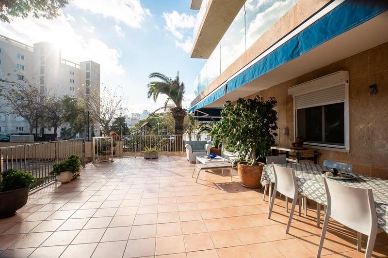 Grande terrasse extérieure avec carrelage en terre cuite, table à manger, salon de jardin et stores bleus.