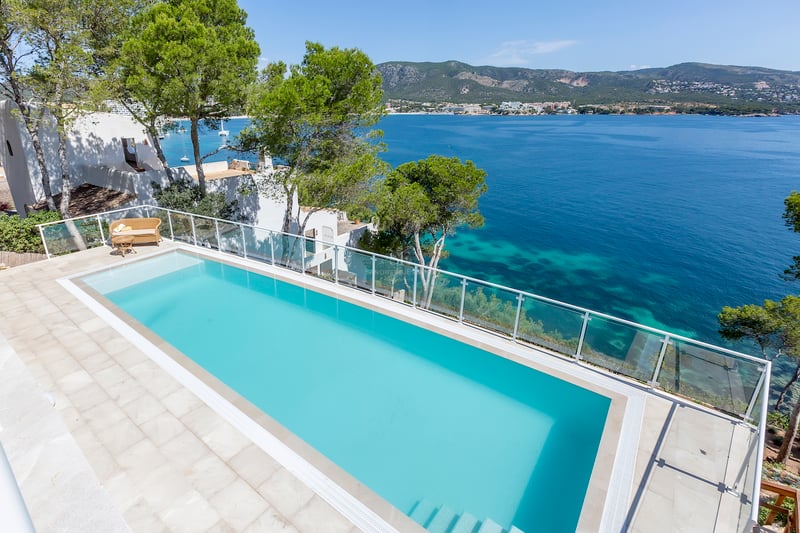 Vue en hauteur d'une piscine à débordement turquoise surplombant la mer Méditerranée avec des montagnes.