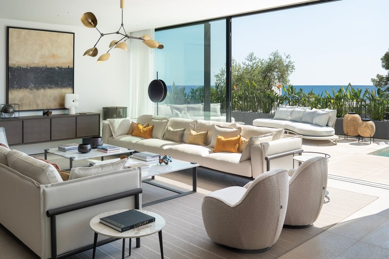 Grand salon contemporain avec canapés blancs, tables en marbre et baies vitrées s'ouvrant sur la mer Méditerranée.