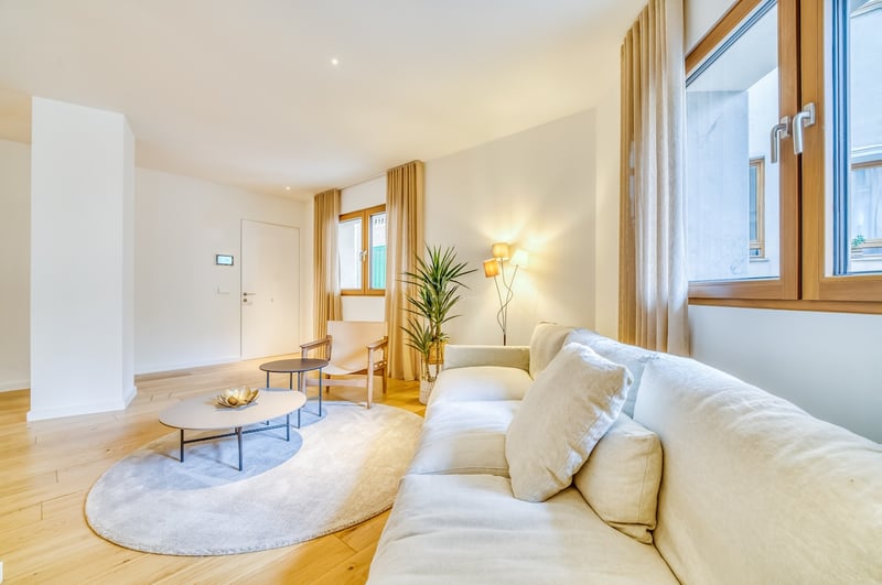 Salon lumineux avec canapé en lin blanc, parquet en chêne, cadres de fenêtres en bois et éclairage chaleureux.