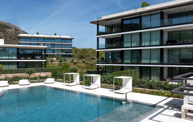 Piscine de luxe avec cabanas blanches devant un immeuble résidentiel contemporain en verre et cadre montagneux.
