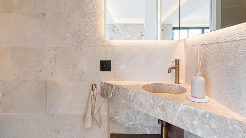 Gros plan d'un lavabo intégré en pierre naturelle avec robinetterie en laiton brossé et miroir rétroéclairé.