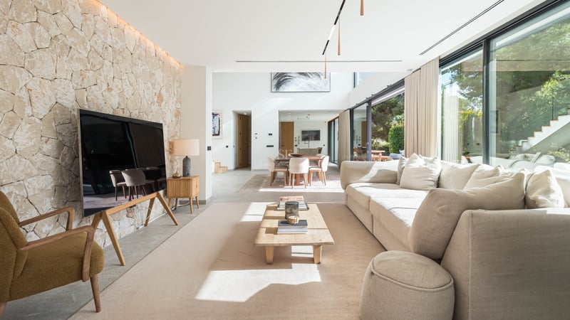 Salon spacieux avec un grand canapé crème, une table basse en bois et un mur d'accent en pierre naturelle claire.