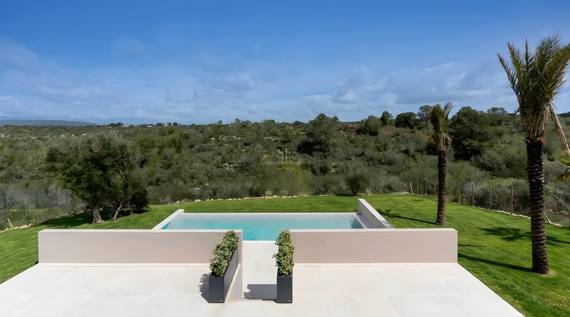 Vue surélevée d'une piscine à débordement avec terrasse en pierre claire dominant des collines verdoyantes.