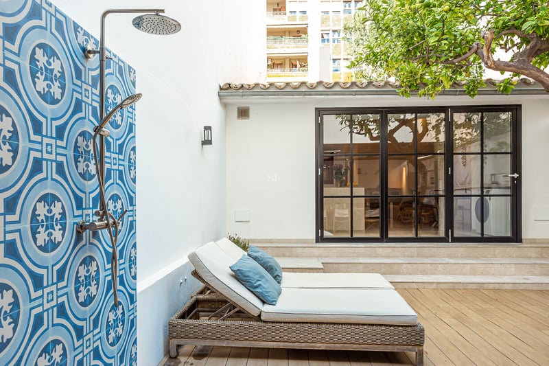 Douche extérieure avec carreaux bleus à motifs à côté de chaises longues sur une terrasse en bois avec un citronnier.