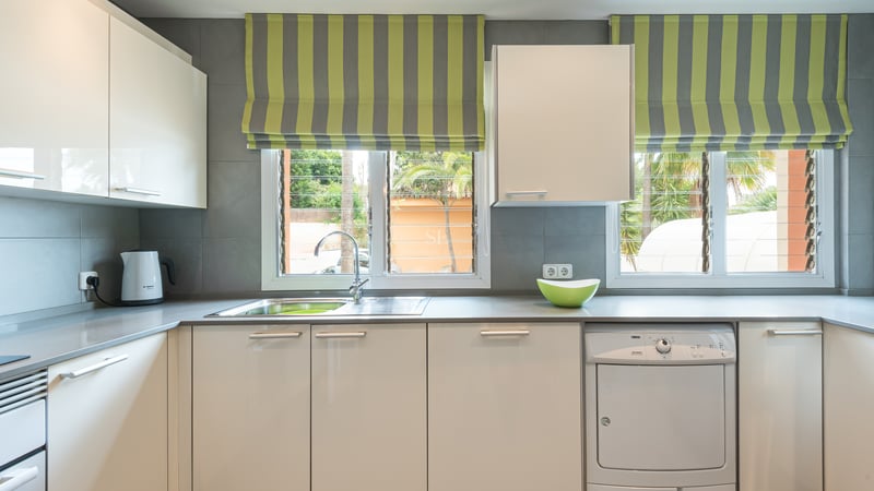 Cuisine contemporaine avec meubles laqués blancs, plans de travail gris et fenêtres donnant sur des palmiers.