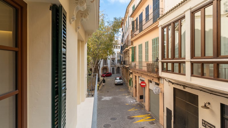 Narrow cobbled street with historic facades and traditional Mediterranean shutters under a clear sky.