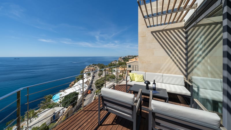 Terrasse en bois avec mobilier de salon gris et garde-corps en verre surplombant la mer Méditerranée.