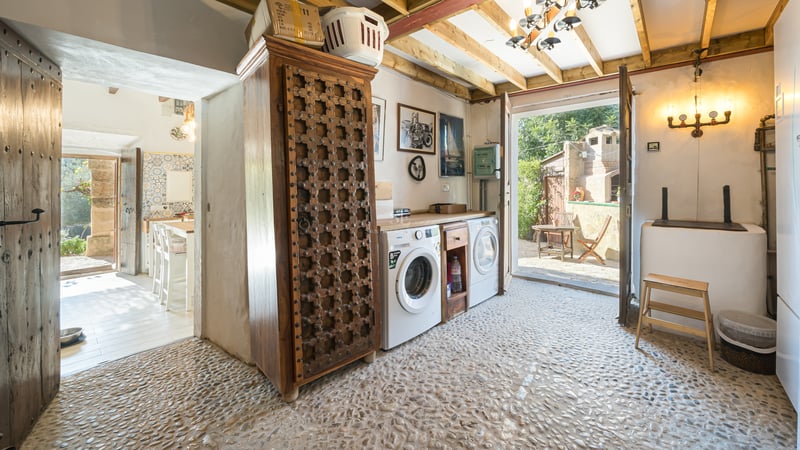 Espace buanderie avec sol en galets, armoire en bois sculpté et accès direct vers l'extérieur.