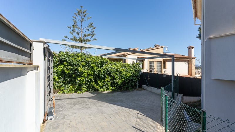 Espace de stationnement pavé avec portail coulissant automatique et structure métallique de pergola.