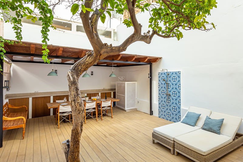 Terrasse en bois avec table à manger sous pergola, grand bain de soleil et douche extérieure carrelée de bleu.