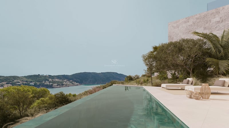 Piscine à débordement sur une terrasse en pierre surplombant une baie turquoise et des collines verdoyantes.
