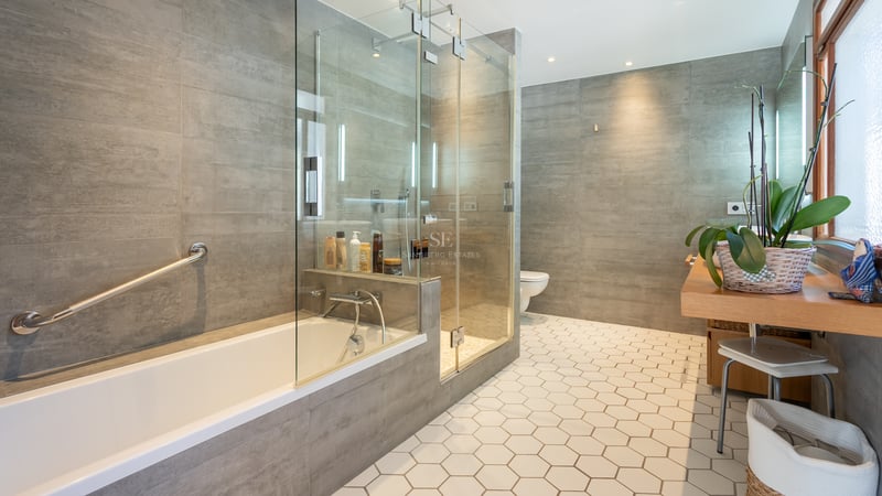 Salle de bain moderne avec carrelage hexagonal blanc, douche vitrée, baignoire et murs gris.