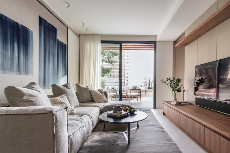 Canapé beige moderne dans un salon ensoleillé avec meubles en bois et grande baie vitrée ouvrant sur une terrasse.