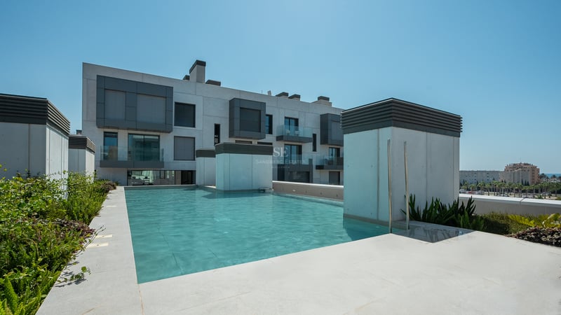 Piscine rectangulaire turquoise sur un toit-terrasse entourée de dalles en pierre et de bâtiments modernes.