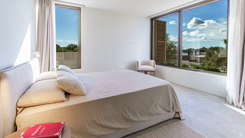 Chambre moderne lumineuse avec grande fenêtre sur jardin, sol en pierre naturelle et lit minimaliste.