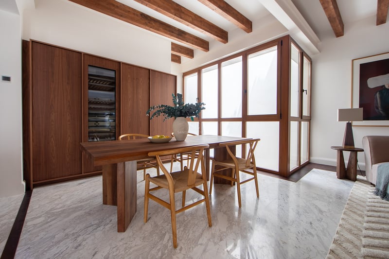 Comedor moderno con suelos de mármol, vigas de madera, mesa de madera maciza y vinoteca integrada en Marbella.