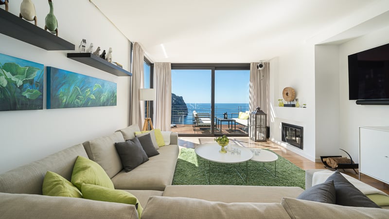 Salon moderne et lumineux avec de grandes baies vitrées ouvrant sur une terrasse vue mer et un canapé d'angle neutre.