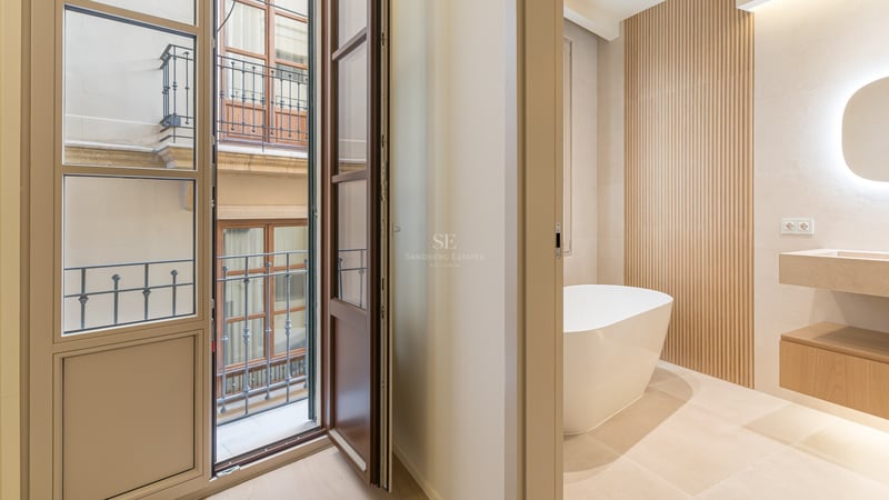 Modern bathroom with white freestanding bathtub, stone vanity, slatted wood wall, and balcony doors opening to a courtyard.