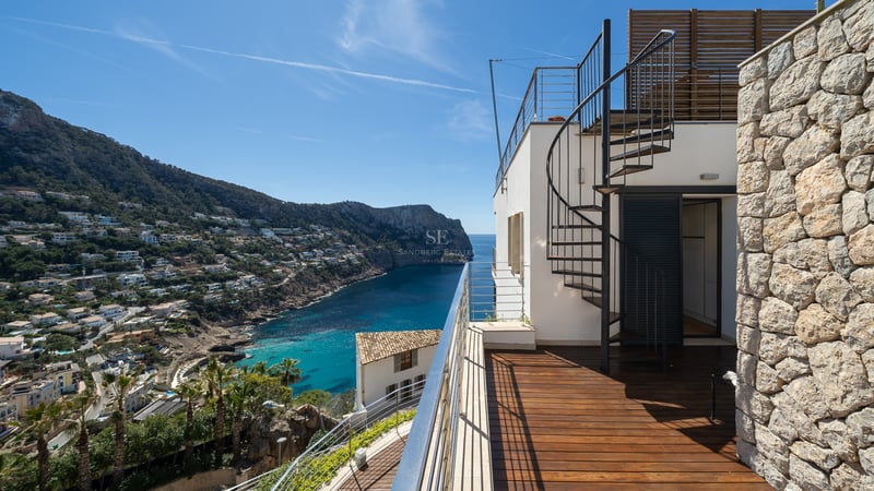 Terrasse avec parquet en bois et escalier en colimaçon surplombant une baie méditerranéenne et des montagnes.
