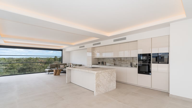 Cuisine blanche minimaliste avec un grand îlot en marbre, appareils intégrés et éclairage de plafond indirect.