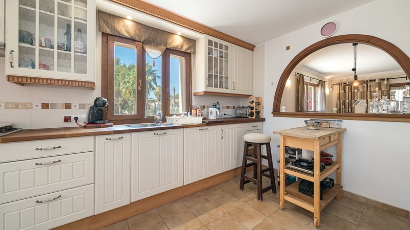 Cuisine crème avec plans de travail en bois, sol en terre cuite et arche donnant sur la salle à manger.