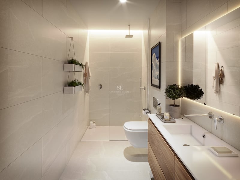 Salle de bain moderne avec carrelage beige, douche vitrée, meuble en bois et miroir rétroéclairé.