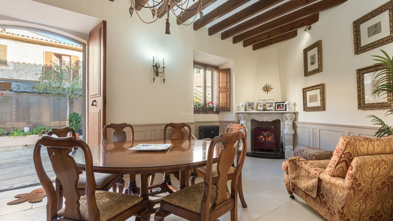 Salle à manger élégante avec table en bois, poutres apparentes et cheminée ornée menant à un patio.