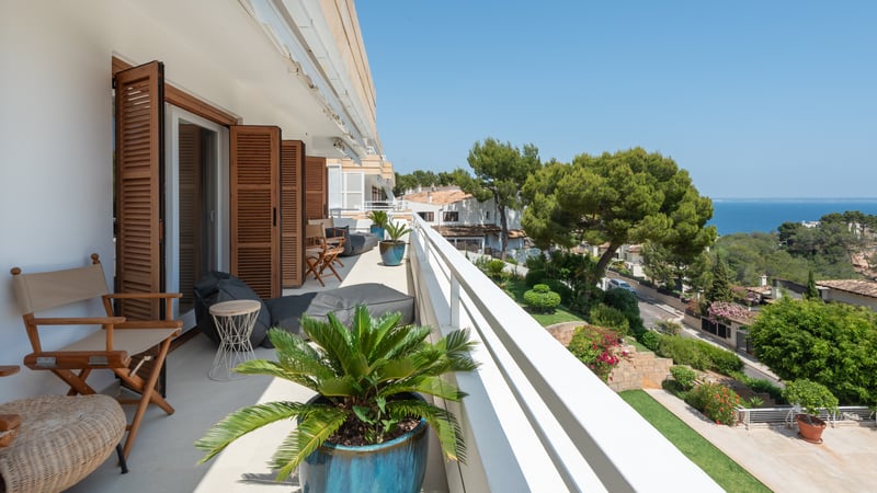 Longue terrasse avec volets en bois, mobilier lounge et vue panoramique sur la mer et la végétation.