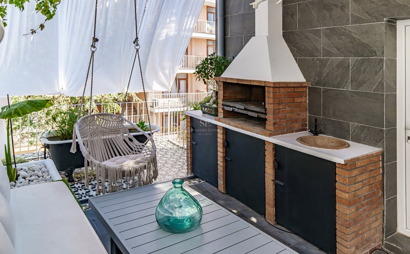 Terrasse moderne avec barbecue en briques, fauteuil suspendu en macramé, table et carrelage décoratif.