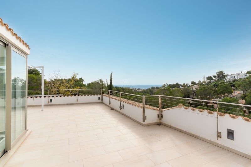 Grande terrasse carrelée avec rambarde métallique offrant une vue dégagée sur la mer et la végétation.