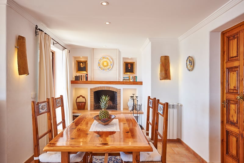 Table à manger en bois et chaises devant une cheminée en brique dans une pièce de style méditerranéen.