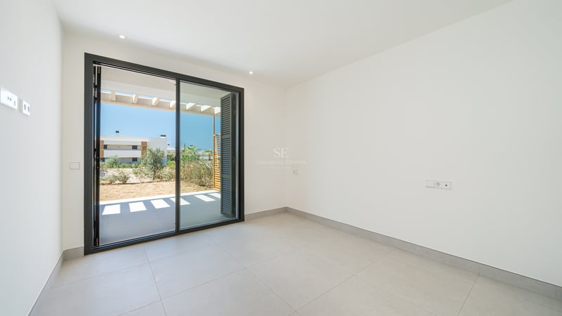 Habitación moderna vacía con paredes blancas, suelo de baldosas grises y gran puerta corredera hacia terraza exterior.