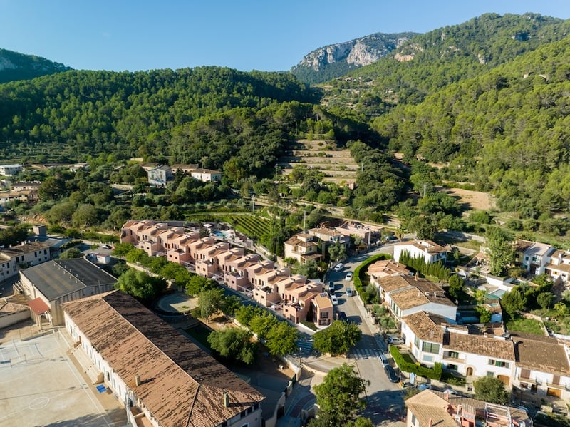 Vue aérienne par drone montrant des maisons modernes en terre cuite dans un village méditerranéen entouré de montagnes.