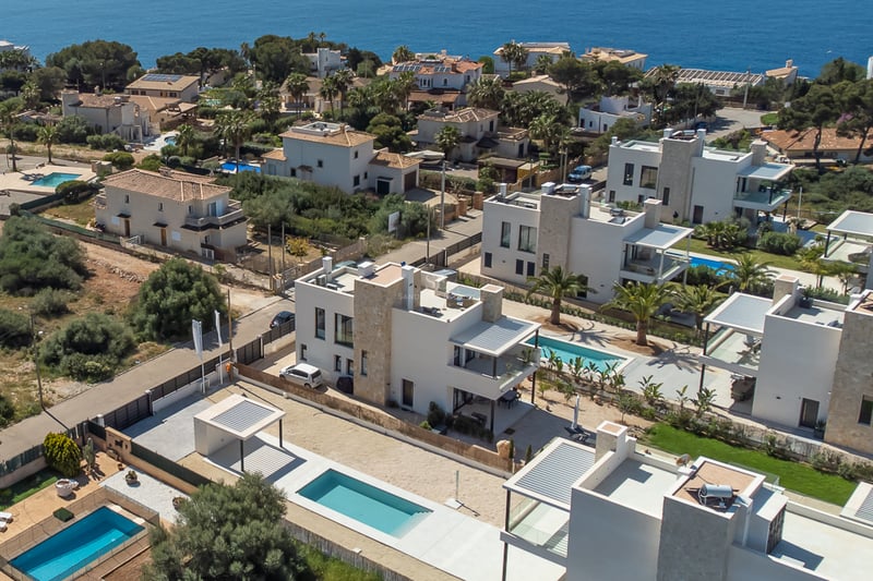 Vue par drone de villas blanches modernes avec piscines privées et accents de pierre dans un quartier côtier méditerranéen.