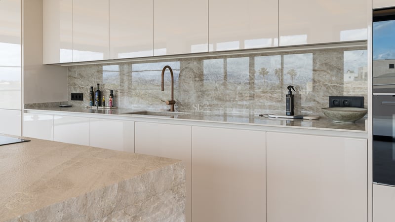 Cuisine contemporaine avec placards crème sans poignées, crédence en marbre veiné et robinetterie design en bronze.