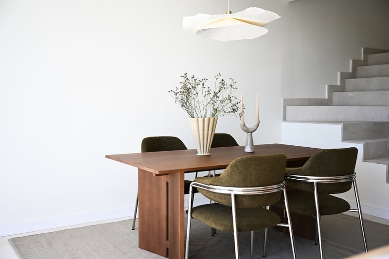 Table à manger en bois, chaises vert olive et suspension design près d'un escalier en pierre claire.