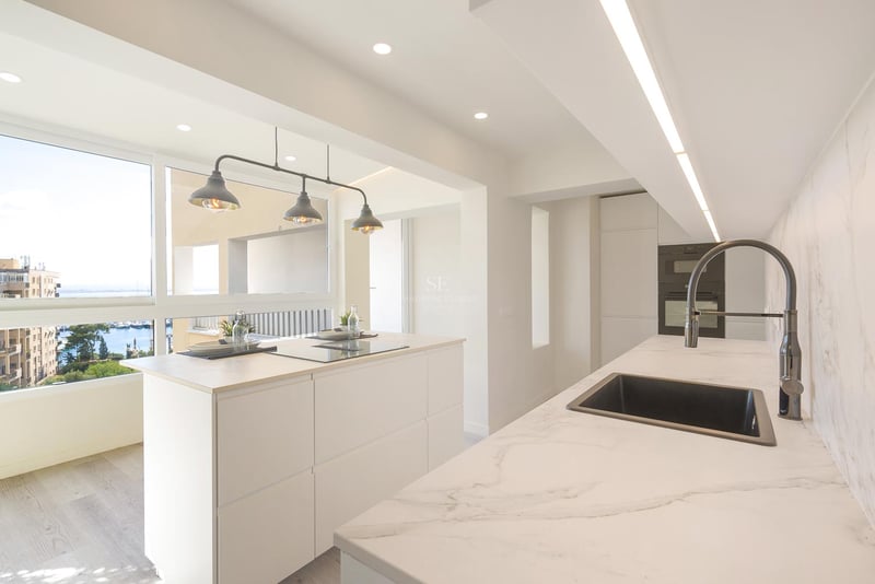 Cuisine moderne lumineuse avec îlot blanc, plans de travail en marbre et fenêtre donnant sur un port de plaisance.