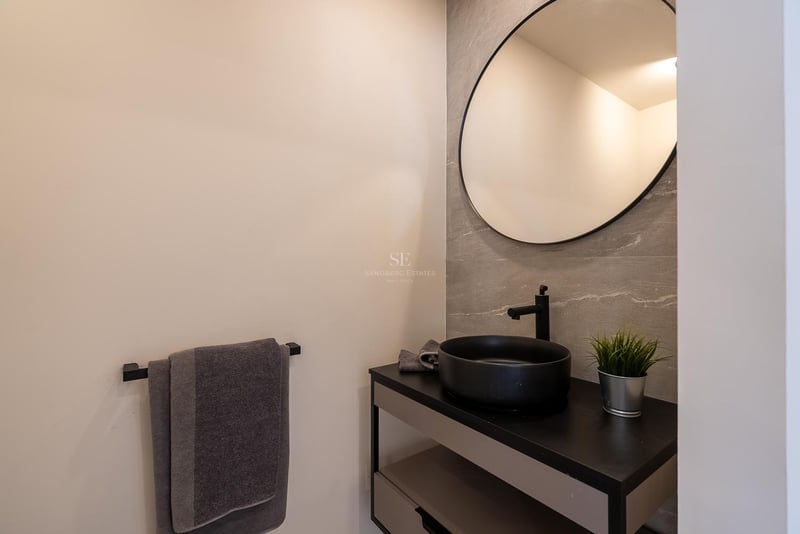 Salle de bains moderne avec miroir circulaire, vasque noire et carrelage mural effet pierre grise.