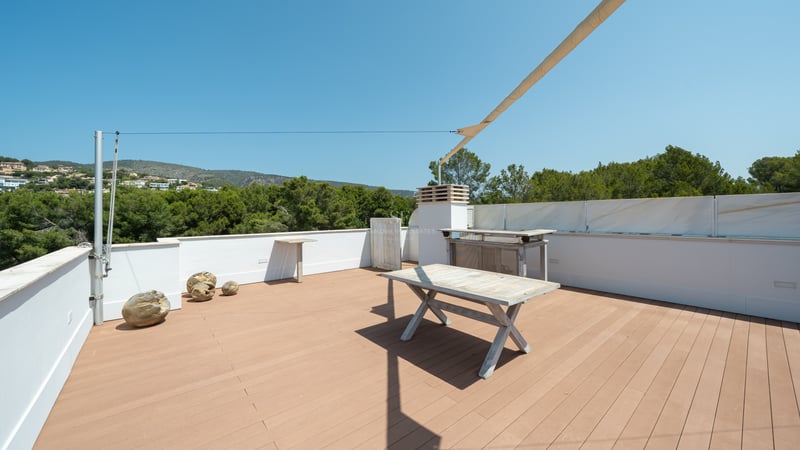 Grande terrasse sur le toit avec plancher en bois, murs blancs, table en bois et voile d'ombrage.
