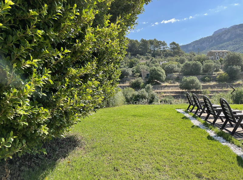 Pelouse verdoyante avec bains de soleil noirs offrant une vue sur des collines en terrasses et une maison en pierre.